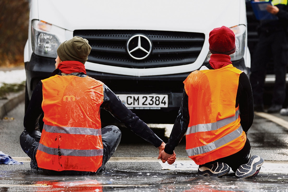 Zwei Menschen in orangenen Westen kleben vor einem Auto