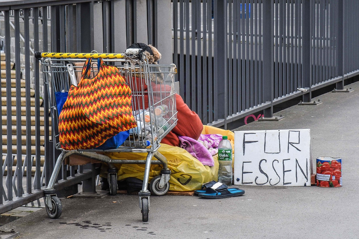 Ein Obdachloser sitzt mit seiner Habe an den Landungsbruecken in Hamburg auf dem Boden.Vor sich hat eine Dose und Schild gestellt mit der Aufschrift: Fuer Essen