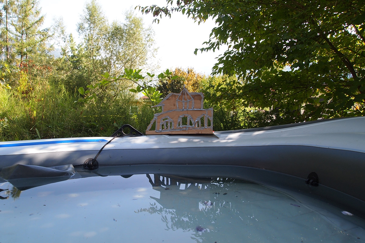 Villa aus Pappe und Panzertape am See (mit Wasser gefülltes Schlauchboot) mit Berg (Erhöhung im Bootrand)