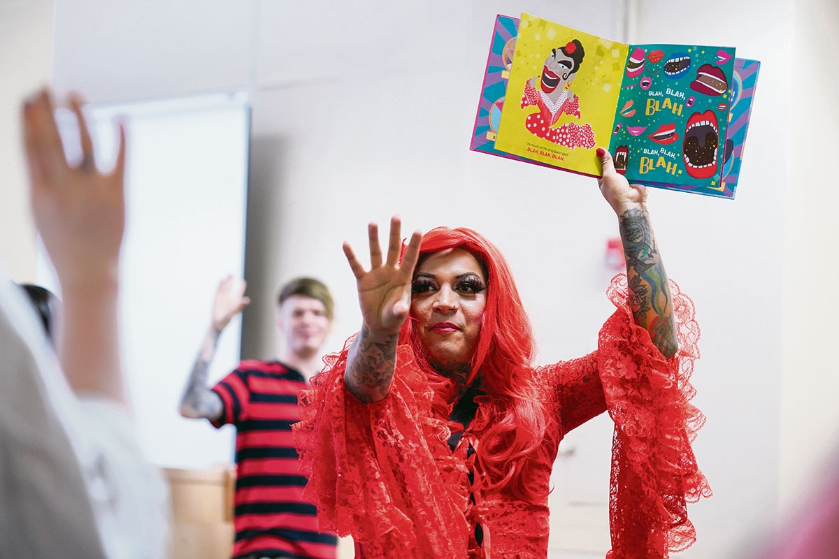 Drag Queen hält ein Kinderbuch hoch auf dem Blah Blah steht