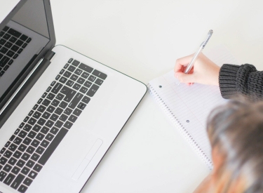 Frau mit Papier, Stift und Laptop in Aufsicht