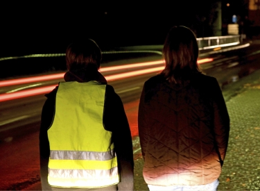 Zwei Personen stehen im Dunklen am Straßenrand, eine trägt eine Warnweste