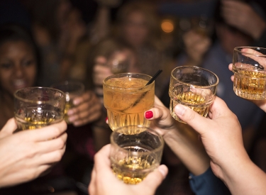 Partysituation, mehrere Hände mit Drinks im Hintergrund Köpfe