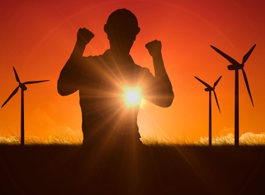 Silhouette einer Person mit Bauhelm vor Windrädern im Sonnenuntergang