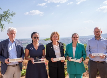 Fünf Personen posieren mit Baumodellen in einer Landschaft