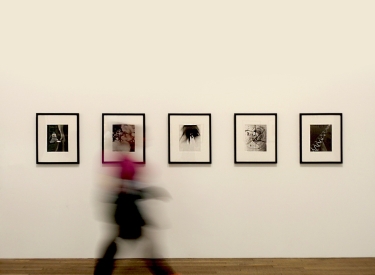 Eine Person läuft in einer Ausstellung an vier Bildern vorbei