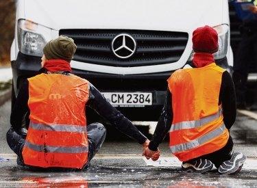 Zwei Menschen in orangenen Westen kleben vor einem Auto