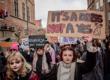 Person zeigt auf Demozug Schild mit der Aufschrift "It's a dress not a yes"